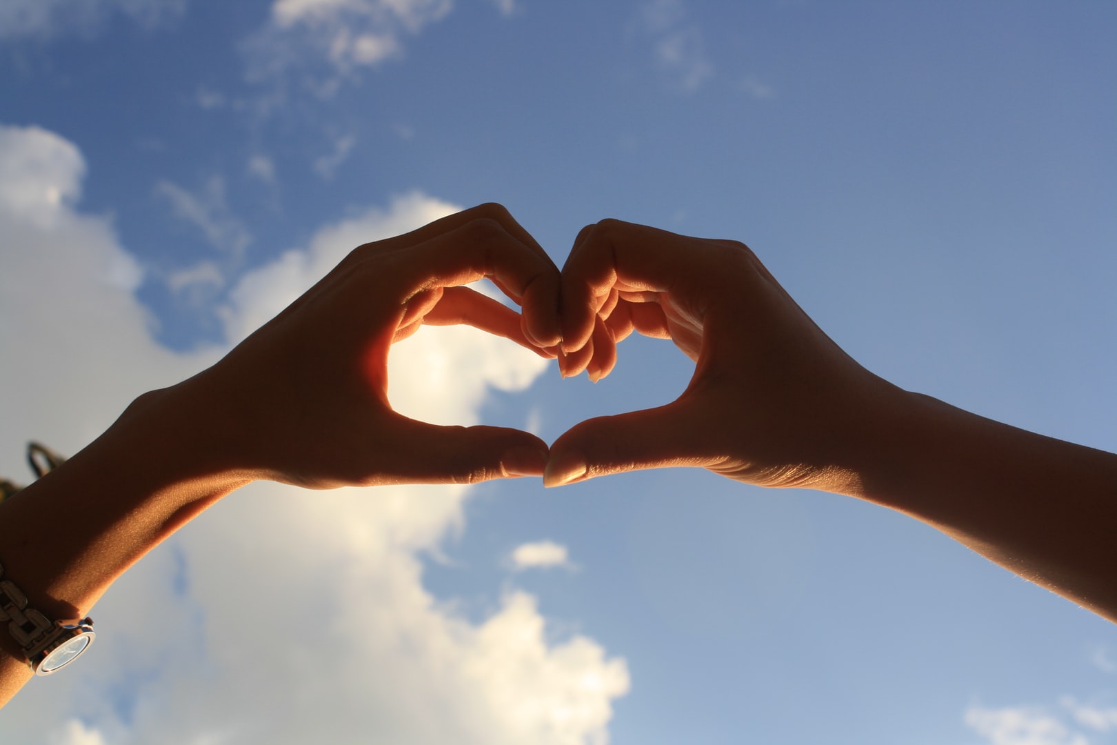 A photo of hands making a heart shape with blue sky in the background
