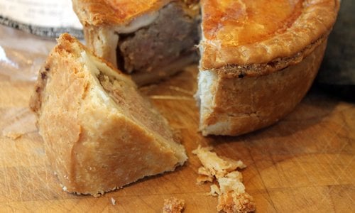 Photo of a pork pie with a quarter section laid on a wooden board