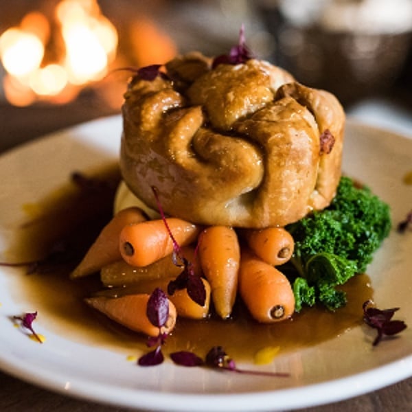 A photo of a Fleece Inn Bretforton pie, sitting on a bed of mash, cabbage & carrots, surrounded with gravy