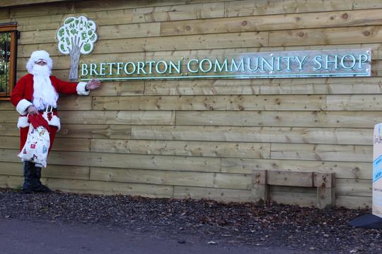 A photo of Santa Claus pointing to the Bretforton Community Shop sign outside the Shop