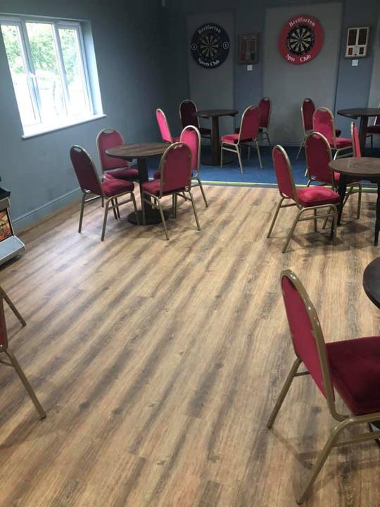 A photo of the interior of Bretforton Sports Club showing chairs and tables and dartboards on the wall in the background