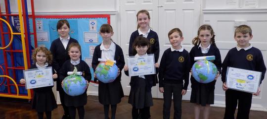 A group of Bretforton Village School pupils posing in the school hall holding globes of the earth and certificates