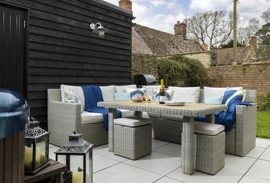 A photo of an outdoor table, sofa and stools, with lanterns outside a Bretforton holiday cottage