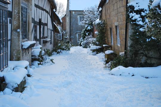 A photo of snow lying on the ground between The Fleece and an old cottage in Bretforton