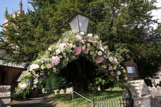 A photo of an arch decorated with flowers at the gate of St Leonard's church Bretforton