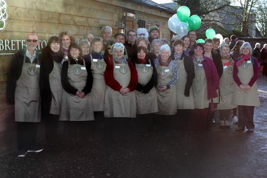 A photo of Bretforton Community Shop volunteers posing outside the Shop wearing their volunteer aprons