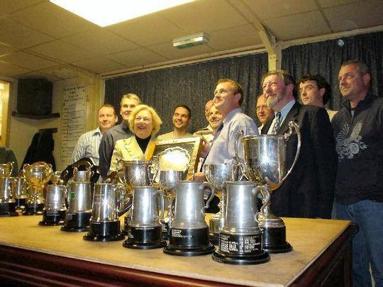 A photo with victorious team members from Bretforton's parish games team with a line of trophies in the foreground on a table