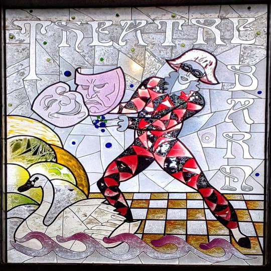A photo of a stained glass window at Bretforton showing a jester with two theatrical theatre masks